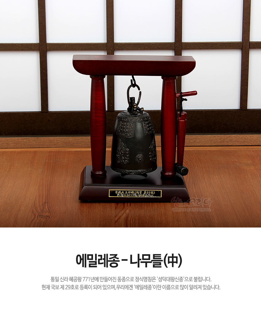 [텍스트: 에밀레종 - 나무틀(中) · 통일 신라 혜공왕 771년에 만들어진 동종으로 정식명칭은 ‘성덕대왕신종’으로 불립니다. 현재 국보 제 29호로 등록이 되어 있으며, 우리에겐 ‘에밀레종’이란 이름으로 많이 알려져 있습니다.] 짙은 적갈색 목재틀과 청동 재질 에밀레종 미니어처, 정교한 연꽃·당초문 장식과 금속 타종봉 조합의 전통 종 모형 장식