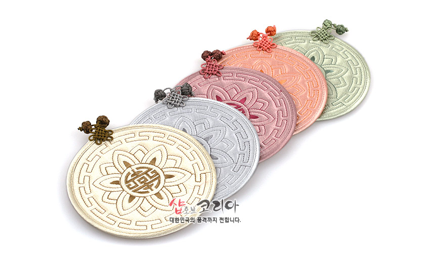 [텍스트: 샵오브코리아 대한민국의 품격까지 전합니다.] 파스텔톤 오방색 원형 누비 컵받침 세트, 연꽃과 수복문 양각 누비 문양과 컬러 매듭 장식이 특징인 패브릭 공예품