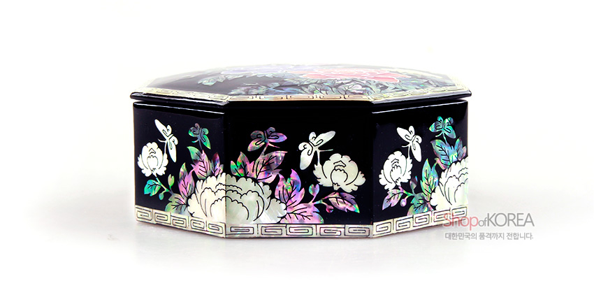 [텍스트: shopofKOREA 대한민국의 품격까지 전합니다.] 흑색 옻칠 바탕에 자개 상감 기법으로 목단꽃과 나비, 잎사귀 문양을 섬세하게 장식한 팔각 보석함 모습