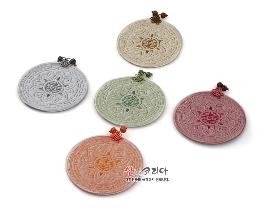 [텍스트: 샵오브코리아 대한민국의 품격까지 전합니다.] 파스텔톤 원형 누비 컵받침, 연꽃과 수복문 문양, 상단 전통 매듭 장식 패브릭 공예품