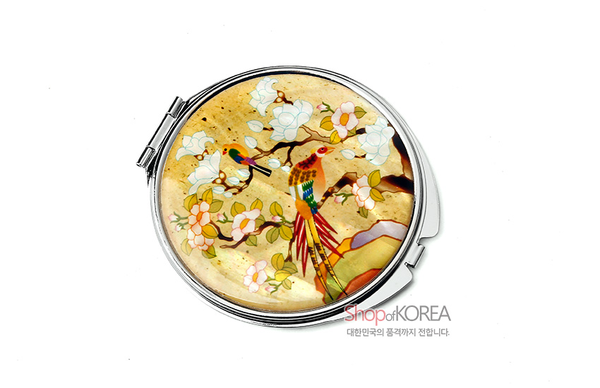 [텍스트: Shop of KOREA / 대한민국의 품격까지 전합니다.] 노란 바탕 위 자개 상감 기법으로 표현한 화조도 문양, 다채로운 색상의 새와 매화가 조화를 이루는 원형 금속 손거울 디자인