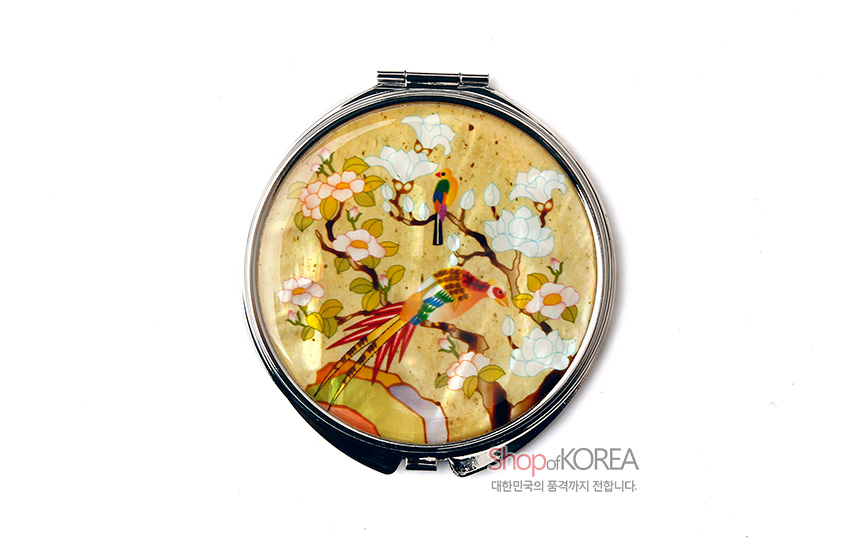 [텍스트: ShopofKOREA 대한민국의 품격까지 전합니다.] 노란 바탕 위 자개 상감 기법으로 표현된 화조채색 문양, 금속 테두리 원형 손거울 디자인