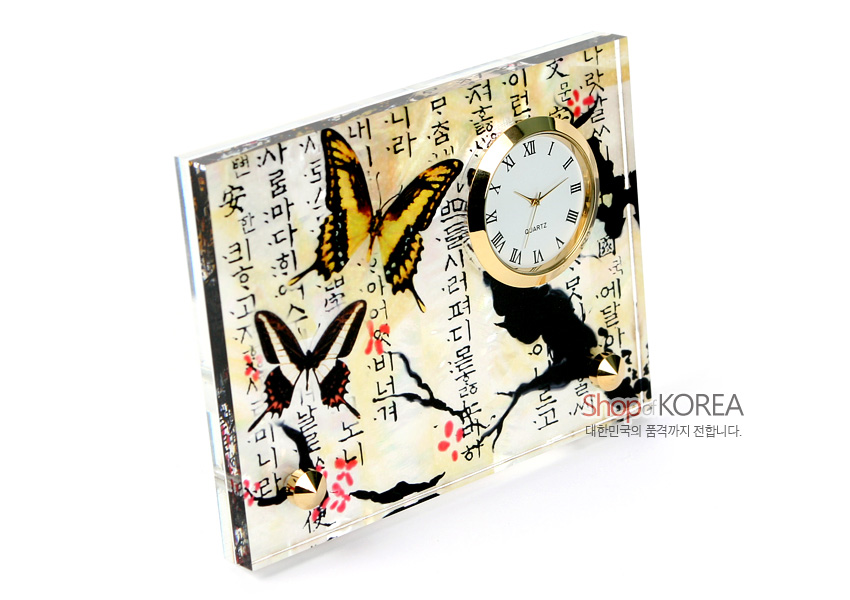 [텍스트: 나랏말싸미 듕귁에 달아 문자와로 서로 사맛디 아니할쎄] 투명 아크릴 속 자개 느낌 배경에 매화 가지와 나비 문양, 한글 서체가 어우러지고 금속 테두리 원형 시계를 더한 탁상용 시계 디자인