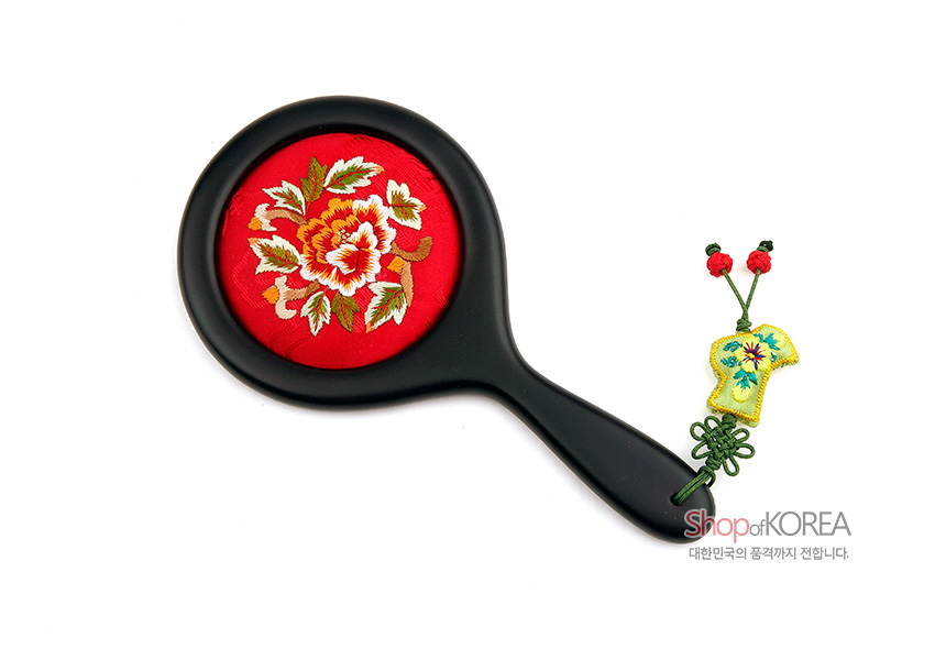 [텍스트: Shop of KOREA 대한민국의 품격까지 전합니다.] 붉은 비단 바탕에 모란 자수를 놓은 원형 손거울과 흑색 손잡이, 조개옷 매듭과 노랑색 비단 복주머니 노리개 장식 구성