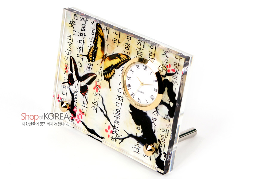 [텍스트: Shop of KOREA, 대한민국의 품격까지 전합니다.] 아크릴 재질 위 자개 느낌 광택과 매화나비, 매화 가지, 한글 서체가 어우러진 금속 테두리 로마자 시계 장식 이미지