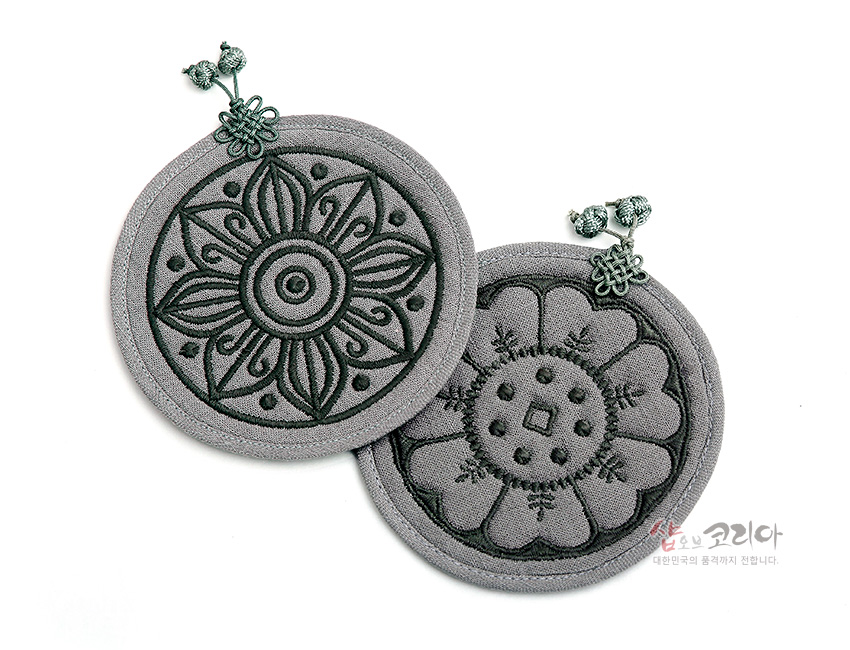 [텍스트: 샵오브코리아 대한민국의 품격까지 전합니다.] 회색 누비 천 위에 고구려·백제 수막새 연꽃 문양을 짙은 실로 자수한 원형 컵받침, 매듭 장식 디테일 구성
