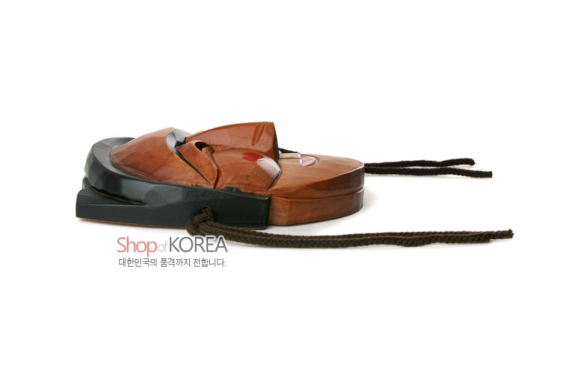 [텍스트: Shop of KOREA 대한민국의 품격까지 전합니다.] 옅은 갈색 원목 조각 위 흑색 머리 장식 대비, 붉은 볼 점과 입술 채색, 짙은 갈색 끈이 연결된 전통 하회 부네탈 옆모습 이미지 설명