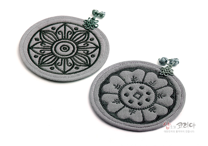 [텍스트: 샵오브코리아 대한민국의 품격까지 전합니다.] 회색 누비 천에 고구려·백제 수막새 연꽃·꽃문양을 자수로 놓고 매듭 장식을 더한 원형 컵받침 2P 세트 이미지 설명