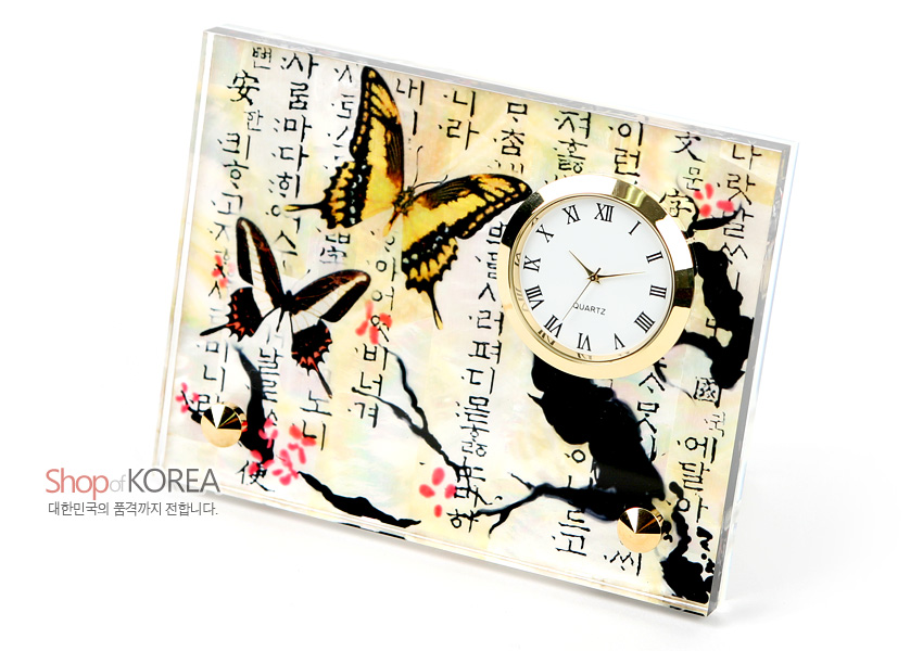 [텍스트: Shop of KOREA 대한민국의 품격까지 전합니다.] 자개 바탕 위에 옻칠 기법으로 매화 가지와 붉은 매화꽃, 노랑·검정색 나비 문양을 표현하고 금속 테두리 원형 시계를 더한 탁상용 시계 이미지