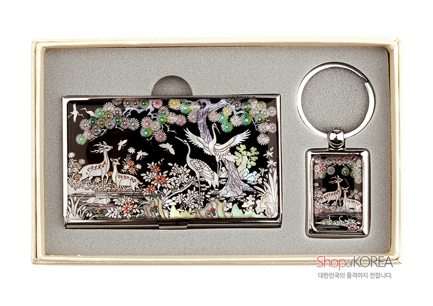[텍스트: Shop of KOREA 대한민국의 품격까지 전합니다.] 흑색 옻칠 바탕 위 자개 상감 기법으로 학·사슴·소나무·국화 장생도 문양을 섬세히 새긴 금속 명함집과 열쇠고리 세트 이미지 설명