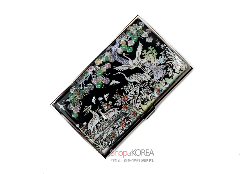 [텍스트: Shop of KOREA 대한민국의 품격까지 전합니다.] 흑색 옻칠 바탕에 자개 상감 기법으로 학과 사슴, 소나무와 꽃 장생도 문양을 섬세하게 장식한 금속 명함집 이미지 설명