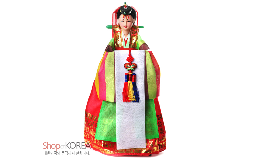 [텍스트: Shop of KOREA 대한민국의 품격까지 전합니다.] 비단 질감 연두·홍색 혼례 한복에 금박 단청 문양, 오방색 술 매듭 노리개와 흰 장삼으로 꾸민 전통 신부 인형 모습