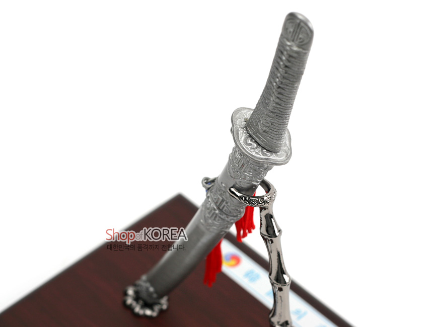 [텍스트: Shop of KOREA 대한민국의 품격까지 전해 드립니다.] 은색 금속 재질 한국도 모형과 음각 문양 칼집, 대나무 형 금속 스탠드, 붉은 술 장식이 어우러진 목제 받침대 위 장식품