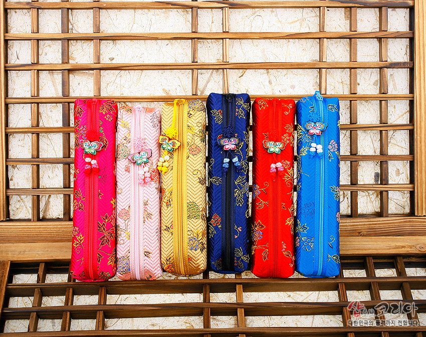 [텍스트: 샵오브코리아 대한민국의 향기를 전세계까지 전합니다.] 오방색 비단 누비 필통, 금색 꽃문양 자수와 나비 매듭 장식 지퍼 손잡이 디자인