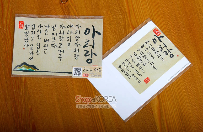 [텍스트: 아리랑 아리랑 아라리요 아리랑 고개를 넘어간다 / 나를 버리고 가시는 님은 십리도 못 가서 발병난다 / 한국의 아침] 한지 질감 베이지 바탕 위 검은 붓글씨 아리랑 가사와 붉은 낙관, 좌하단 수묵 산수 문양 장식 엽서 디자인