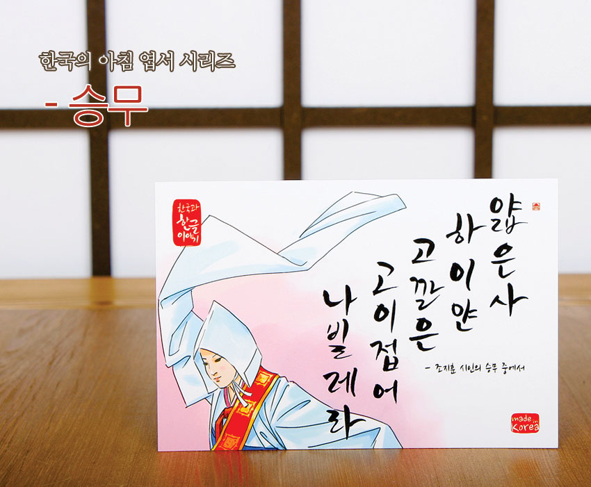 [텍스트: 한국의 아침 엽서 시리즈 승무 / 한국과 한글이야기 / 얇은삿갓 사이로고인눈 나빌레라 - 조지훈 시인의 승무 중에서 / made in Korea] 연분홍 그라데이션 배경에 수묵화풍 승무 무용수와 검은 붓글씨가 조화를 이룬 엽서 이미지 설명