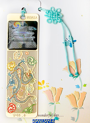 [텍스트: KOREA / 남대문-용 / wonderful day.....] 자개 상감으로 남대문과 용, 구름 문양을 표현한 금속 책갈피와 청색 전통 매듭끈 장식의 조화로운 디자인