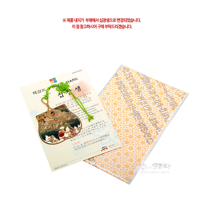 [텍스트: ※ 제품 내지가 부채에서 십장생으로 변경되었습니다. 이 점 참고하시어 구매 부탁드리겠습니다. / BOOK MARK / 십장생 / Made in Korea] 금장 처리된 금속 부채형 책갈피와 연두색 전통 매듭, 십장생 산수와 해·구름을 섬세한 채색으로 표현한 구성