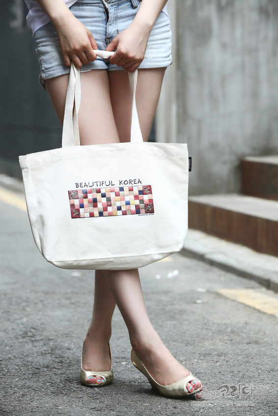 [텍스트: BEAUTIFUL KOREA] 아이보리 면 캔버스 소재 토트백, 색동 문양의 직사각 패턴과 모서리 전통 꽃문양 프린트 장식 모습