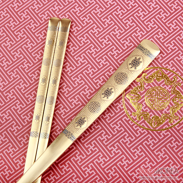 [텍스트: Shop of KOREA] 금빛 티타늄 수저와 젓가락에 십장생과 수자 문양, 기하학 띠무늬를 정교한 음각으로 새긴 전통 금속 공예 디자인