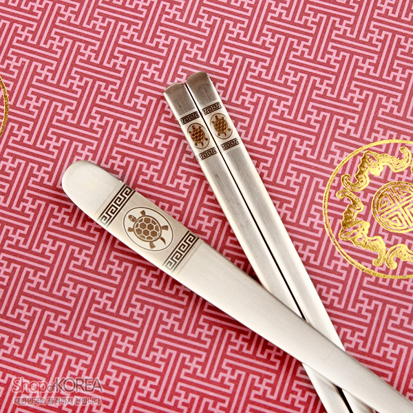 [텍스트: Shop of KOREA] 스테인리스 재질에 거북이 문양과 전통 기하학 무늬를 음각한 젓가락·숟가락 2인 세트, 분홍 바탕 전통 단청 문양 배경 이미지 설명