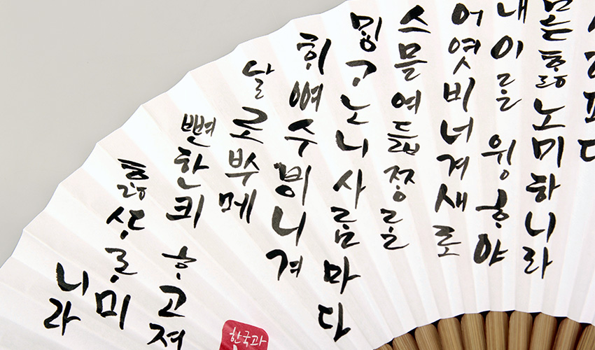 [텍스트: 내 이름은 훈민정음이니라 … 한국의 아침] 흰 한지 접선 위 흑색 먹 훈민정음 캘리그래피와 붉은 전각, 대나무 살이 어우러진 전통 부채 디자인