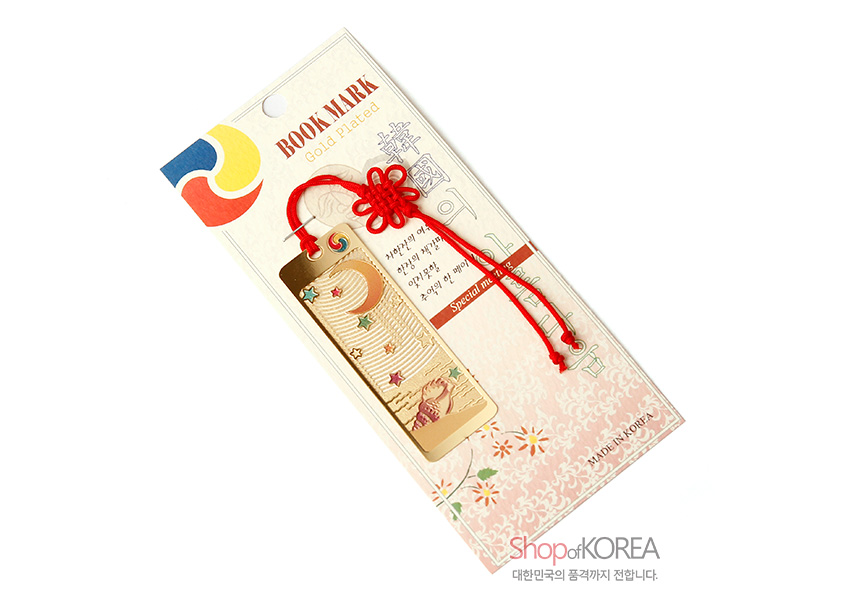 [텍스트: BOOKMARK Gold-plated, MADE IN KOREA, Shop of KOREA 대한민국의 품격까지 전합니다.] 금장 금속 재질에 달과 고동, 별 문양을 양각과 오픈워크로 표현하고 붉은 전통 매듭끈을 더한 직사각 책갈피 이미지 설명