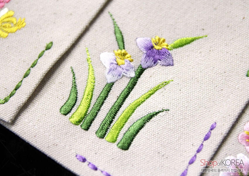 [텍스트: Shop of KOREA, 대한민국의 품격까지 전합니다] 광목 천 위에 연보라색 난초와 초록 잎사귀를 실물감 있게 수놓은 자수 문양 식탁보 디테일 이미지