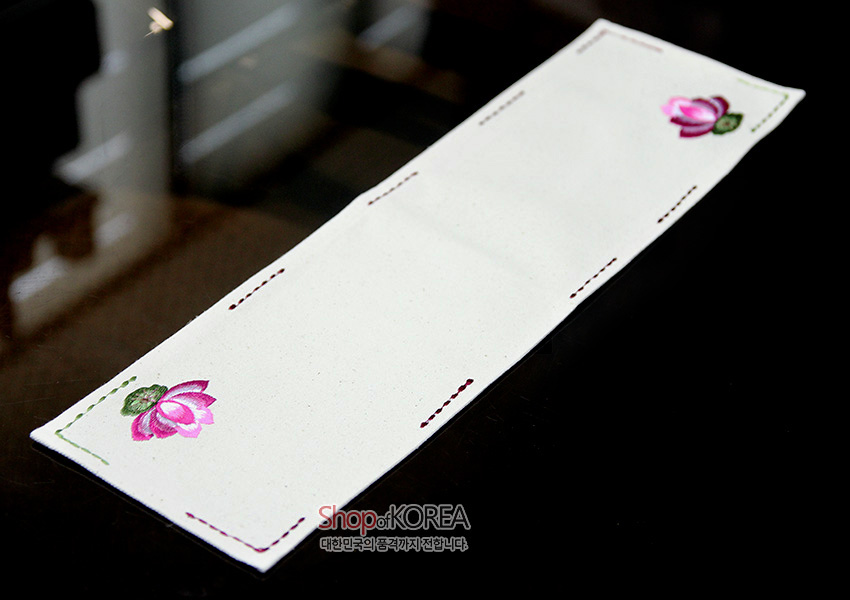 [텍스트: Shop of KOREA 대한민국의 품격까지 전합니다] 아이보리 광목 직사각 식탁보, 양 끝 분홍 연꽃 자수와 가장자리 색실 스티치 장식이 어우러진 디자인