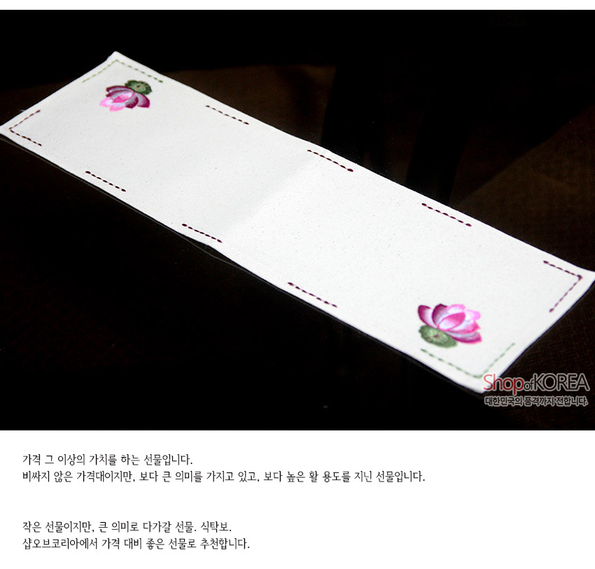 [텍스트: ShopofKOREA 대한민국의 품격까지 전합니다] 광목 소재 아이보리 색 직사각 식탁보, 양 끝 분홍 연꽃 자수와 가장자리 색실 스티치가 포인트인 전통 문양 디자인