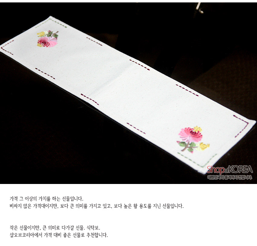 [텍스트: Shop of KOREA 대한민국의 품격까지 전합니다.] 광목 재질 흰색 직사각 식탁보, 가장자리 스티치 자수와 양끝 분홍·노랑 국화 자수 문양이 있는 전통 패브릭 디자인