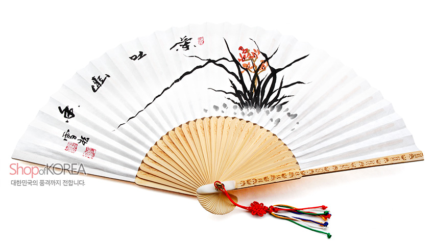 [텍스트: Shop of KOREA / 대한민국의 품격까지 전합니다.] 흰 한지 위 수묵 난초와 한자 서예 문양, 대나무 살대와 가장자리 조각 장식, 붉은 매듭과 오색 술 장식 전통 합죽선 이미지 설명