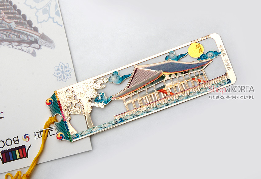 [텍스트: Shop of KOREA, 대한민국의 품격까지 전합니다.] 금장 금속 재질에 경회루와 연못, 소나무와 구름, 해를 다채로운 에나멜 색채로 표현하고 노랑 전통 매듭끈을 더한 책갈피 이미지