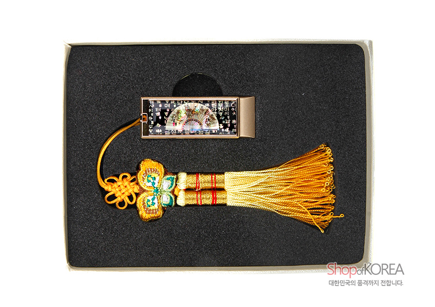 [텍스트: Shop of KOREA 대한민국의 품격까지 전합니다.] 흑색 바탕 금속 USB 위 자개 상감 부채와 훈민정음 문자 문양, 황금색 비단 매듭과 술 장식 구성 이미지