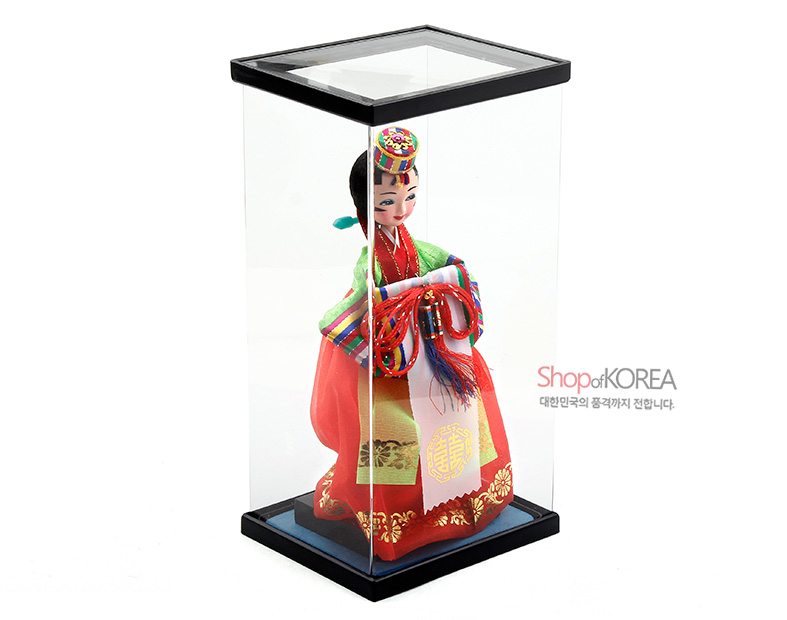 [텍스트: Shop of KOREA 대한민국의 품격까지 전합니다.] 투명 케이스 속 붉은 비단 치마와 금박 단청 문양, 오방색 줄무늬 저고리와 매듭 술 장식이 조화를 이룬 왕비 한복 인형 모습