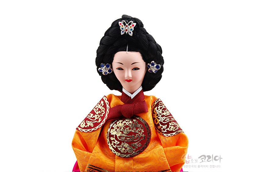 [텍스트: shop of korea] 비단 재질 주황 당의 위 금사 자수의 용 흉배 문양, 붉은 매듭 고름과 화려한 보석 장식 가체 머리 장신구의 한복 인형 모습