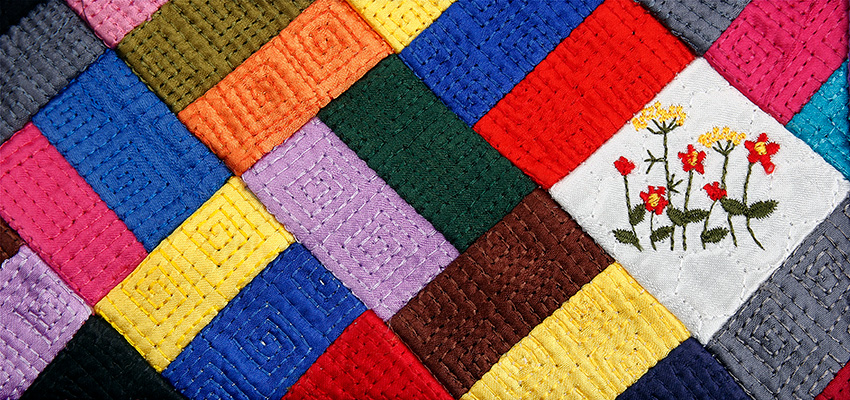 다채로운 색상 천 조각을 누비 기법으로 잇대어 사선 패턴을 이룬 조각보 장식과, 흰색 천 위에 꽃 문양 자수를 놓은 섬세한 누비 파우치 부분 클로즈업 이미지