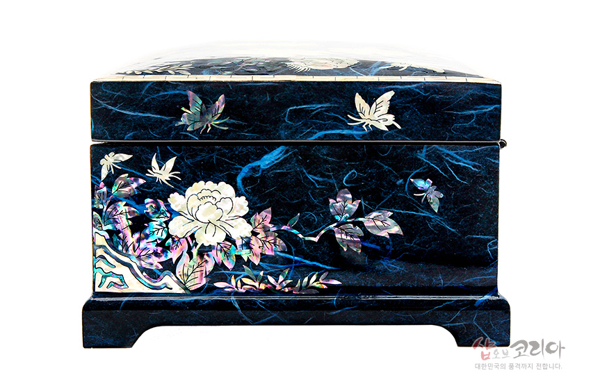 [텍스트: 샵오브코리아 대한민국의 품격까지 전합니다.] 짙은 청색 옻칠 바탕 위에 자개 상감으로 목단과 나비, 꽃잎 문양을 정교하게 표현한 직사각형 보석함 정면 모습