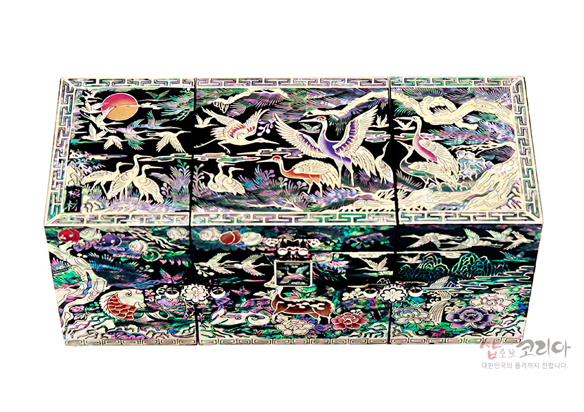 [텍스트: 샵오브코리아 대한민국의 품격까지 전합니다.] 흑색 옻칠 바탕에 자개 상감 기법으로 학과 해·구름·송, 장생도 문양을 다채로운 오색으로 섬세하게 표현한 3폭 쌍합 보석함 디자인