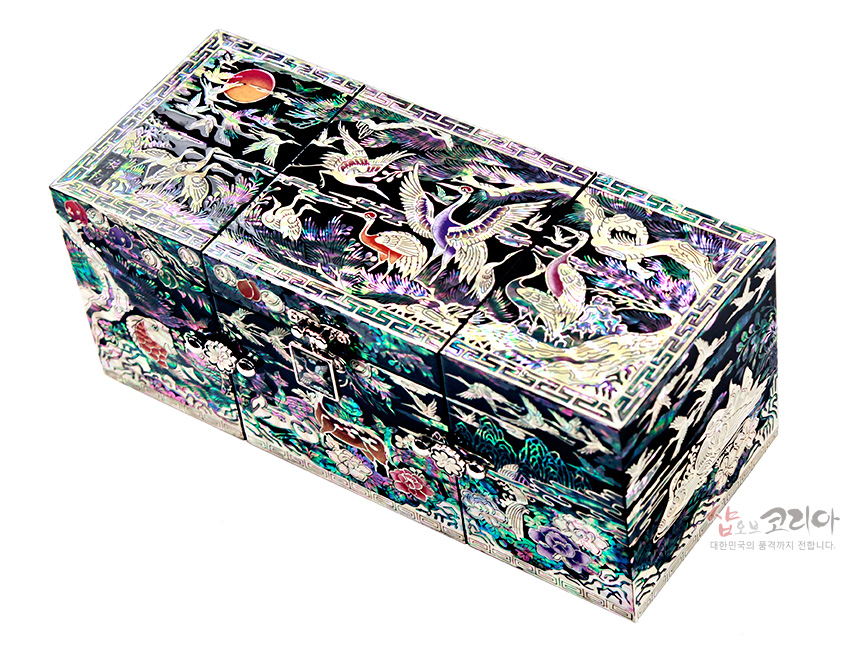 [텍스트: 샵오브코리아 대한민국의 품격까지 전합니다.] 흑색 옻칠 바탕 위 화려한 자개 상감 기법으로 장생도와 학, 구름, 해, 송림 문양을 섬세하게 장식한 3폭 쌍합 보석함 이미지 설명