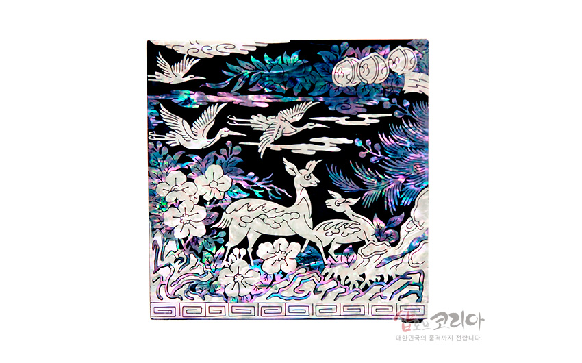 [텍스트: 샵오브코리아 대한민국의 품격까지 전합니다.] 흑색 옻칠 바탕 위 자개 상감 기법으로 장생도 풍경의 사슴, 학, 소나무와 구름, 꽃문양을 화려하게 표현한 보석함 전면 장식 이미지