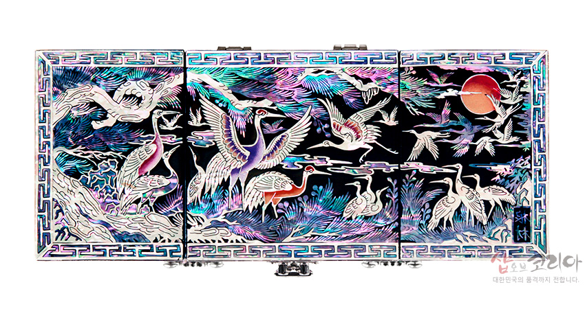 [텍스트: 샵오브코리아 대한민국의 품격까지 전합니다.] 흑색 옻칠 바탕에 자개 상감 기법으로 학과 소나무, 구름, 붉은 해, 번와문 테두리를 화려한 오색 광택으로 표현한 3폭 쌍합 보석함 정면 모습