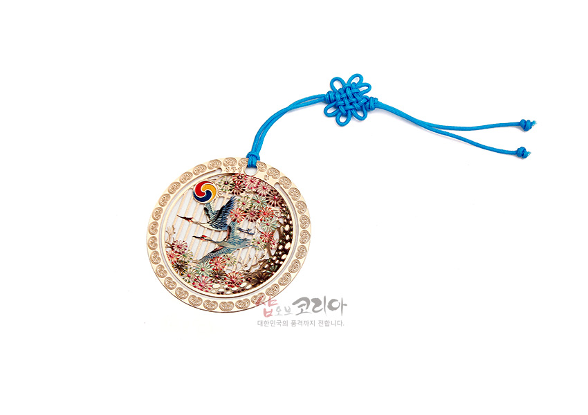 [텍스트: 샵오브코리아 대한민국의 품격까지 전합니다.] 금색 금속 원형 테두리에 자개 상감 기법으로 십장생 학과 꽃, 태극 문양을 섬세하게 표현하고 청색 전통 매듭 끈으로 장식한 책갈피 이미지 설명