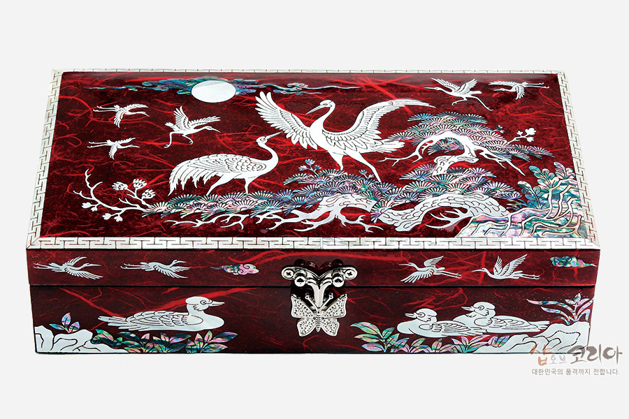 [텍스트: 샵오브코리아 대한민국의 품격까지 전합니다] 붉은 옻칠 바탕에 자개 상감 기법으로 학과 소나무, 구름, 연꽃, 기러기 문양을 섬세하게 장식한 직사각형 보석함
