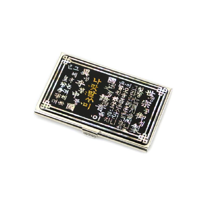 검은 바탕 위에 금속 테두리와 모서리 장식, 훈민정음 한글 글귀 문양이 새겨진 금속 명함집.