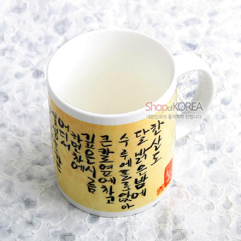 연한 노란 바탕 위에 검은 한글 서예 문양이 인쇄된 도자기 머그컵.