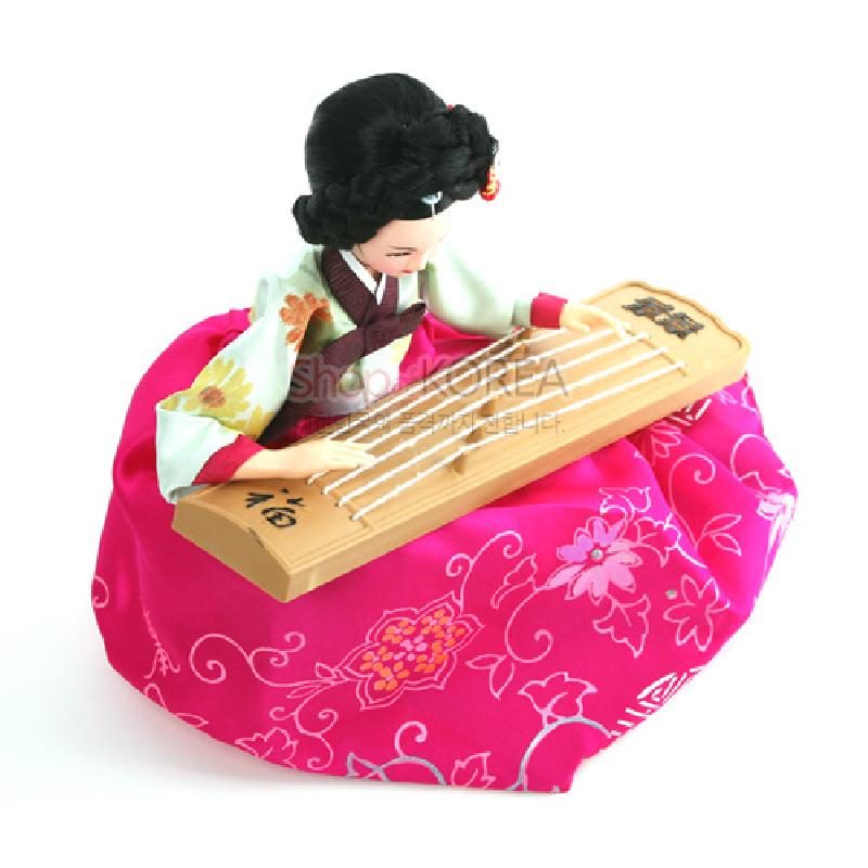 분홍색 비단 치마와 꽃무늬 문양이 돋보이는 한복 차림, 나무 재질 가야금을 연주하는 전통 복식 인형.