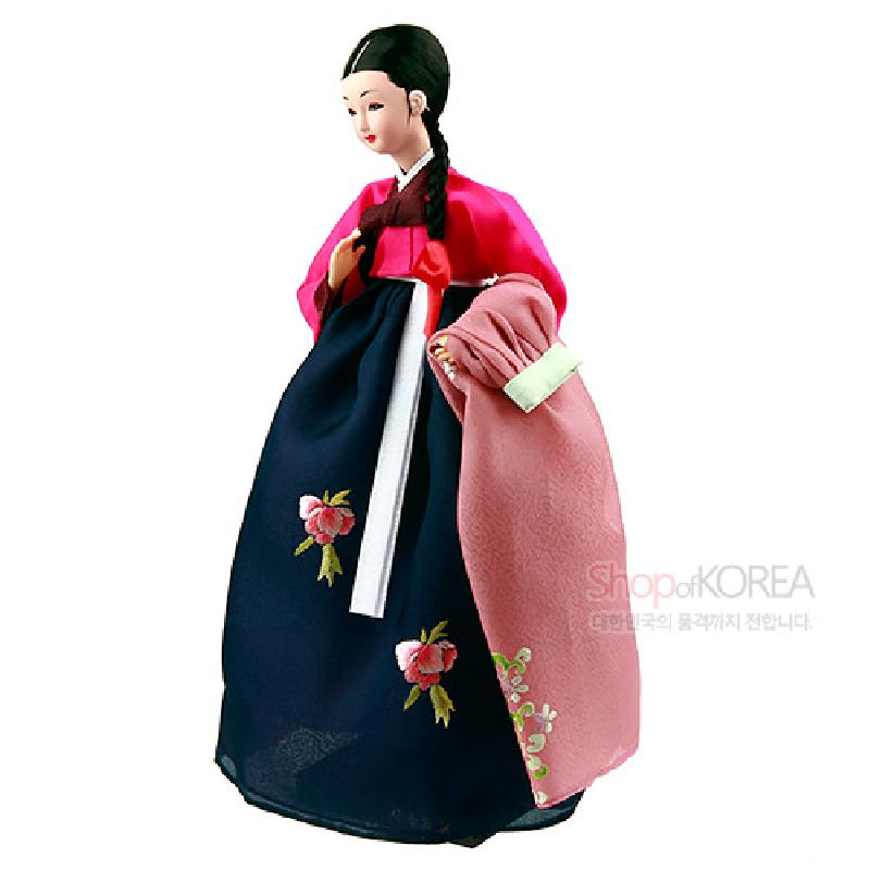 짙은 남색 치마와 분홍 저고리, 장식 자수와 전통 매듭 보자기가 특징인 한복 인형.