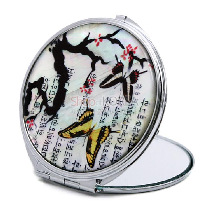 자개 바탕 위에 옻칠로 그린 매화 가지와 나비, 한글 서예 문양이 어우러진 원형 금속 손거울.