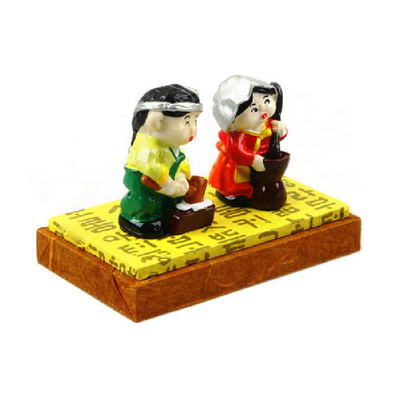 한글 문양이 인쇄된 노란 받침 위에 채색된 한복 차림 절구 남매 인형을 올린 수지 소재 장식품.